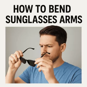 A young man with dark brown hair and a trimmed beard is focused on adjusting the arms of his black wayfarer sunglasses. He is wearing a casual blue T-shirt and applying pressure to the hinges, set against a light gray background. The image includes bold text above reading, "HOW TO BEND SUNGLASSES ARMS."
