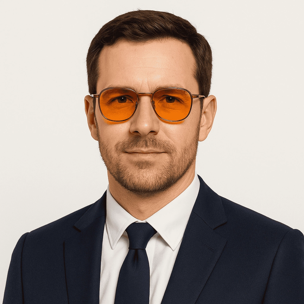 A professional-looking man wearing a navy suit and white shirt, sporting orange-tinted aviator sunglasses, against a simple white background.