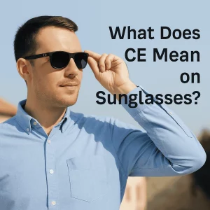 A fair-skinned man in his early 30s with brown hair and light stubble, wearing black sunglasses with a visible CE mark. He is adjusting the glasses with a slight smile, dressed in a light blue shirt. The background features a soft blue sky and a blurred building. Bold text beside him asks, 'What Does CE Mean on Sunglasses?'